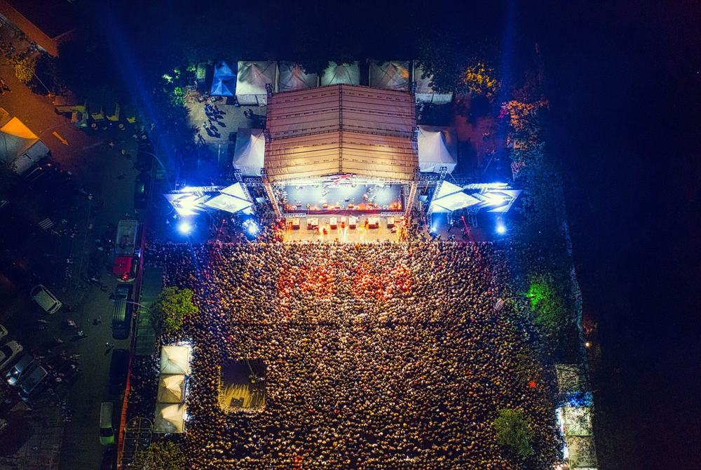 Scena festiwalowa nocą w kolorowych światłach, widok z daleka zza publiczności