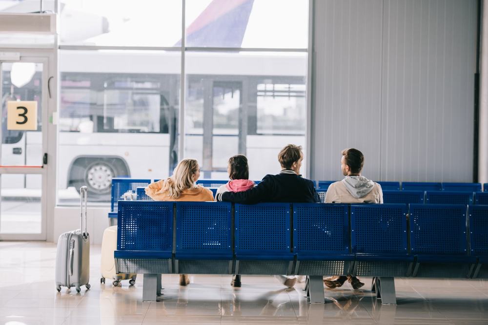 Rozmyta tablica odlotów na lotnisku i czekający podróżni widoczni od tyłu